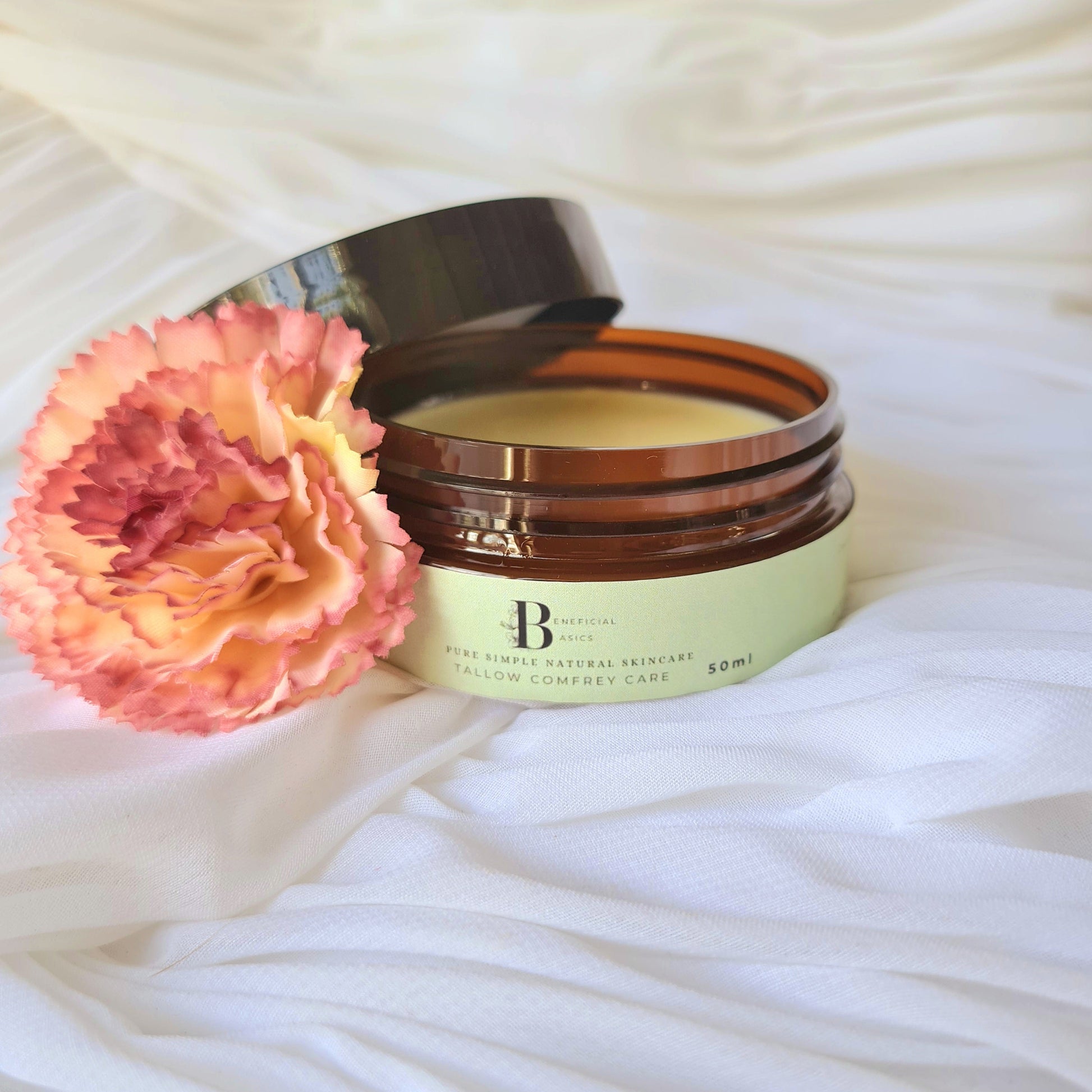 Open jar of beef tallow comfrey cream with a pink flower on a white textured surface
