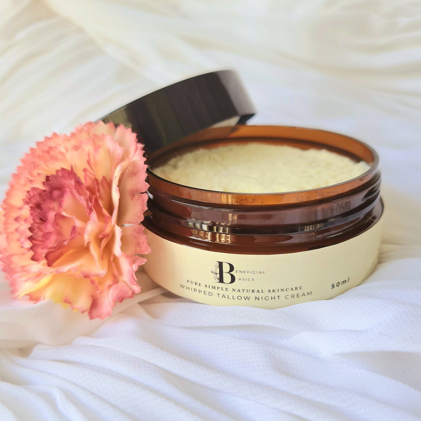 Jar of beef tallow whipped face cream with a pink flower on a white fabric background